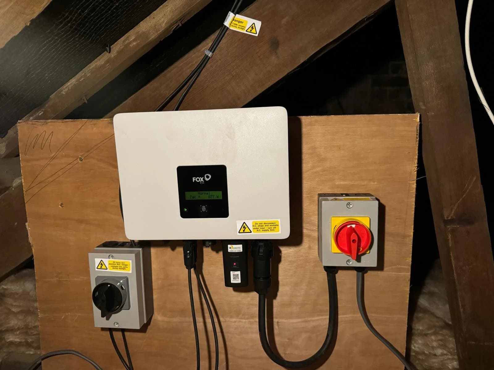 A FoxESS inverter with isolator switches mounted on a board in the loft