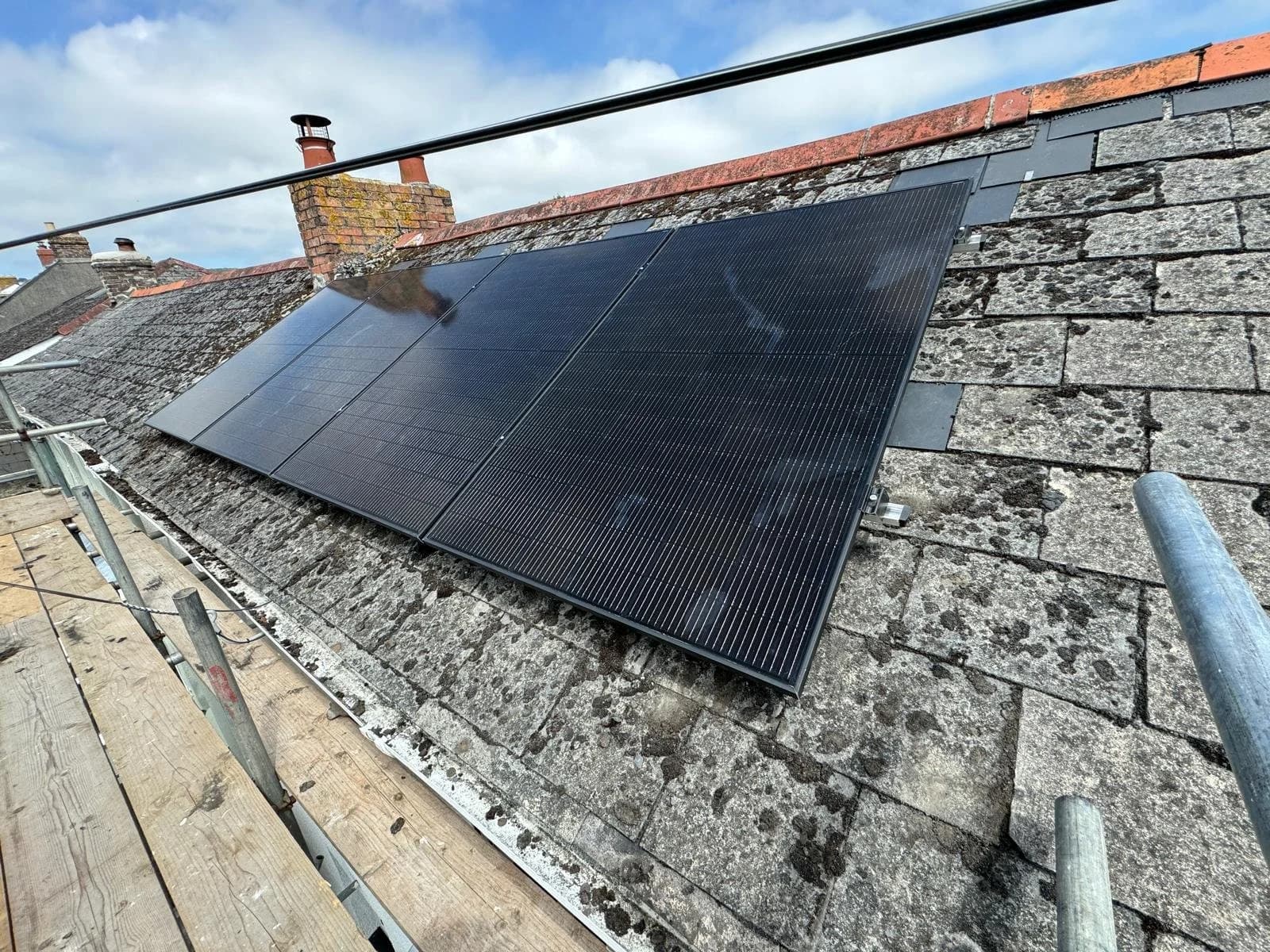 Black solar panels fitted on a slate roof in Clifden, St Austell, with scaffolding below